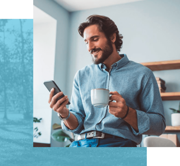 eine Person im Jeanshemd hält eine Kaffeetasse und schaut lächelnd auf ein Smartphone